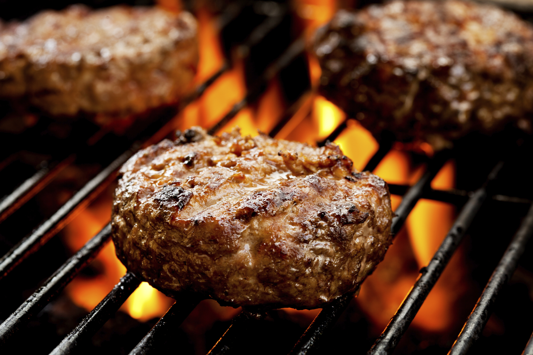 Close up of three burgers on the grill